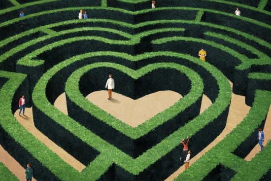An illustration of a heart-shaped maze made from green hedges. Several small human figures walk through the labyrinth, some alone and others in pairs, searching for paths through the twists and turns. At the center, a person stands alone on a heart-shaped patch of open ground. The scene evokes themes of love, searching, and the complexities of modern relationships.